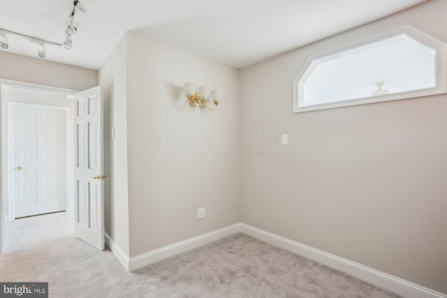 spare room with track lighting and light carpet