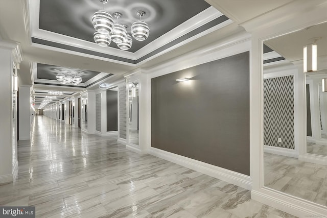 corridor featuring decorative columns, ornamental molding, a raised ceiling, and a chandelier