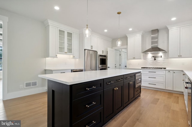 kitchen featuring white cabinets, light hardwood / wood-style flooring, a kitchen island, and wall chimney range hood