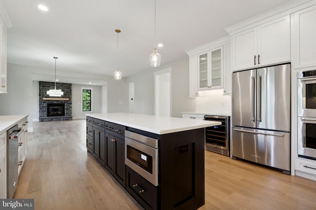 kitchen with hanging light fixtures, a fireplace, white cabinetry, stainless steel appliances, and beverage cooler