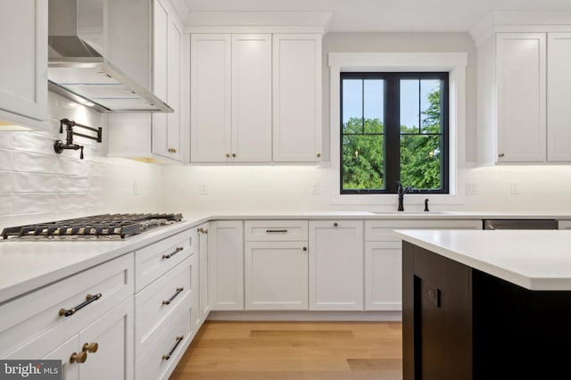 kitchen with white cabinetry, sink, and wall chimney range hood