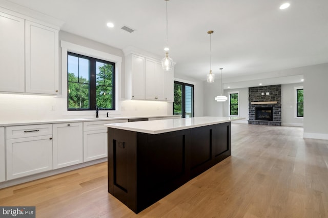 kitchen with white cabinets, a center island, a stone fireplace, and pendant lighting