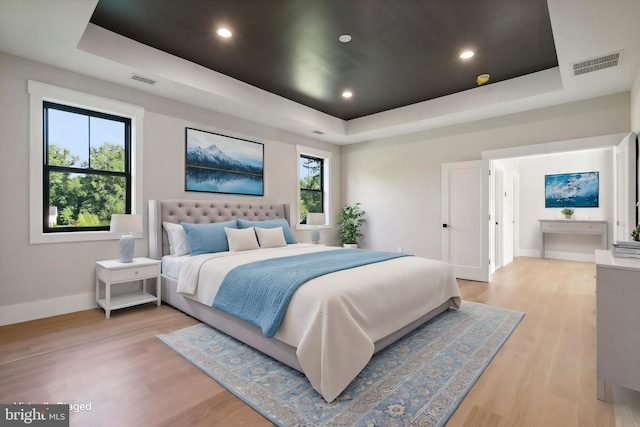 bedroom featuring ensuite bath, light hardwood / wood-style flooring, and a tray ceiling