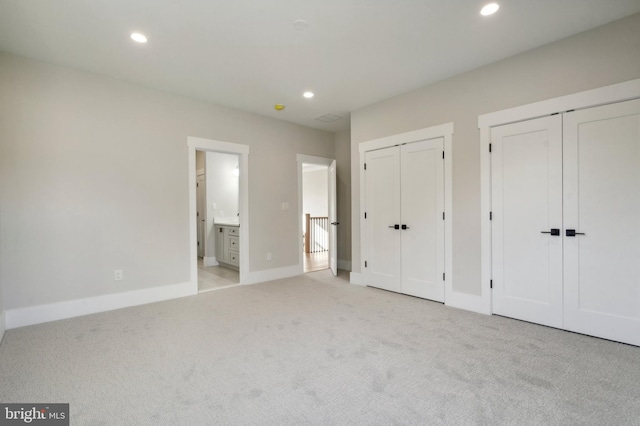 unfurnished bedroom featuring connected bathroom, multiple closets, and light colored carpet