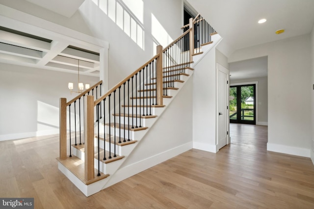 staircase featuring beamed ceiling, a notable chandelier, hardwood / wood-style flooring, and coffered ceiling