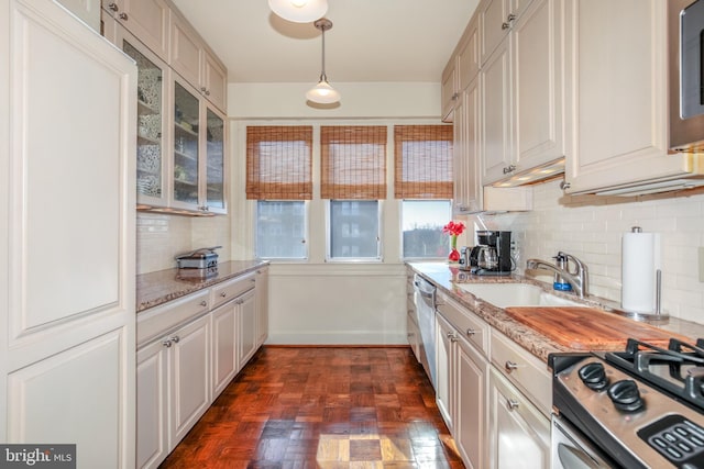 kitchen with pendant lighting, dark parquet flooring, sink, light stone counters, and stainless steel appliances