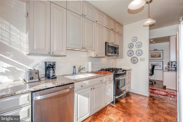 kitchen featuring sink, stainless steel appliances, light stone counters, pendant lighting, and light parquet flooring