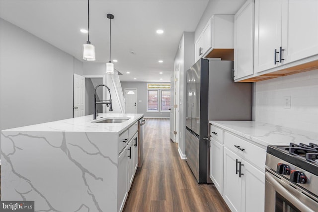 kitchen with light stone countertops, white cabinetry, sink, stainless steel appliances, and a kitchen island with sink