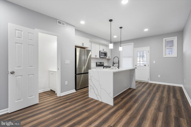 kitchen featuring appliances with stainless steel finishes, dark wood-type flooring, pendant lighting, a center island with sink, and white cabinets