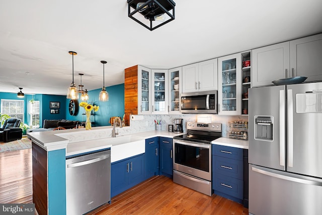 kitchen featuring pendant lighting, blue cabinetry, white cabinetry, kitchen peninsula, and stainless steel appliances