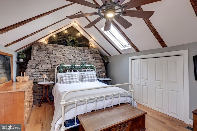 bedroom with ceiling fan, a closet, lofted ceiling with skylight, and light wood-type flooring