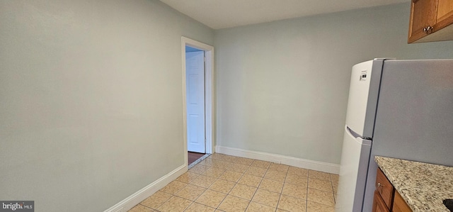 kitchen featuring white refrigerator, light tile patterned flooring, and light stone countertops