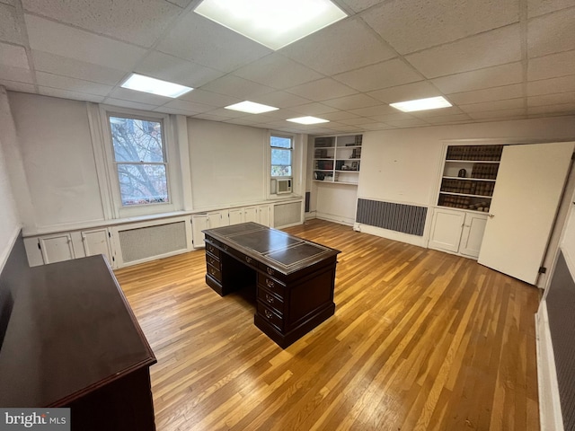 home office with light wood-type flooring, built in features, and a drop ceiling