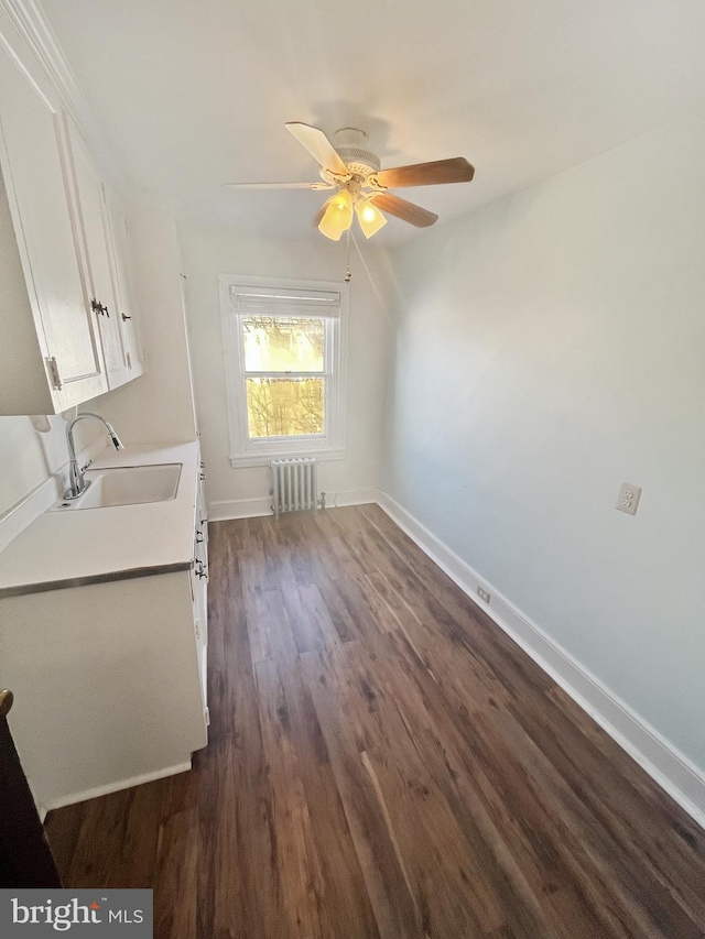 interior space with radiator, ceiling fan, sink, dark hardwood / wood-style flooring, and white cabinets