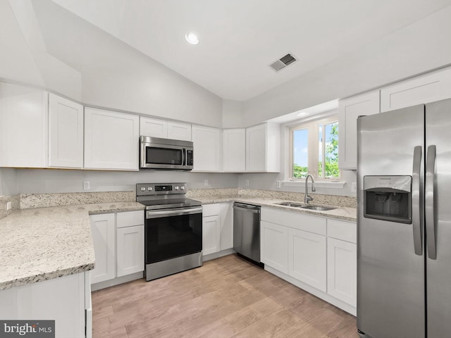 kitchen featuring appliances with stainless steel finishes, vaulted ceiling, sink, light hardwood / wood-style flooring, and white cabinetry