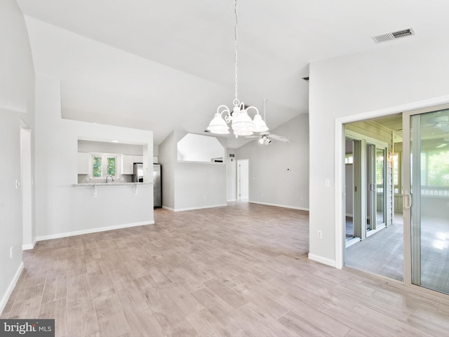 unfurnished living room featuring plenty of natural light, ceiling fan with notable chandelier, vaulted ceiling, and light wood-type flooring