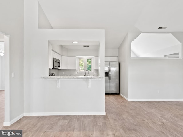 kitchen featuring white cabinetry, stainless steel appliances, light hardwood / wood-style flooring, kitchen peninsula, and a breakfast bar area