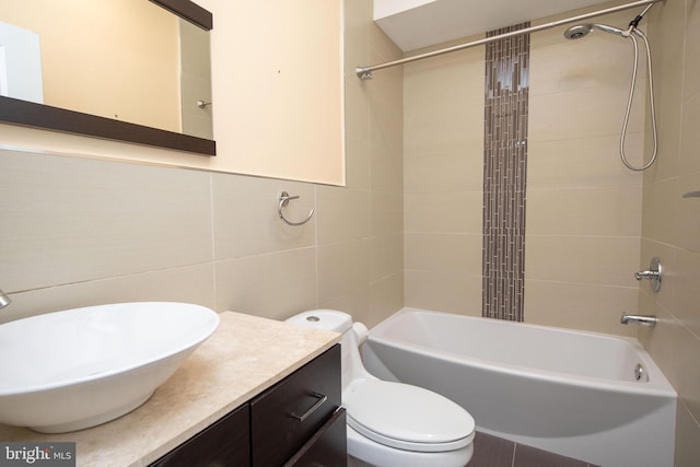 full bathroom featuring tiled shower / bath, vanity, toilet, and tile walls