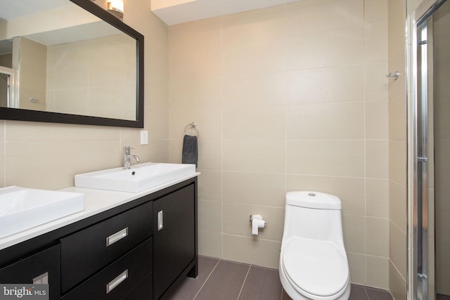 bathroom featuring vanity, toilet, tile walls, and a shower with shower door