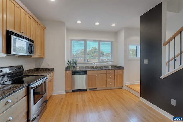 kitchen featuring light brown cabinetry, dark stone counters, stainless steel appliances, sink, and light hardwood / wood-style flooring