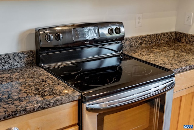 kitchen featuring dark stone countertops, stainless steel electric range oven, and light brown cabinetry