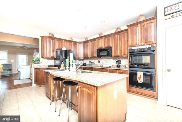 kitchen featuring sink, light stone countertops, a breakfast bar, an island with sink, and black appliances