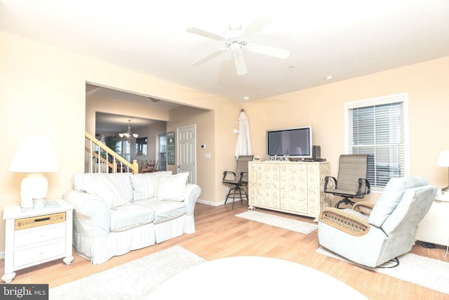 living room with ceiling fan with notable chandelier and light hardwood / wood-style flooring