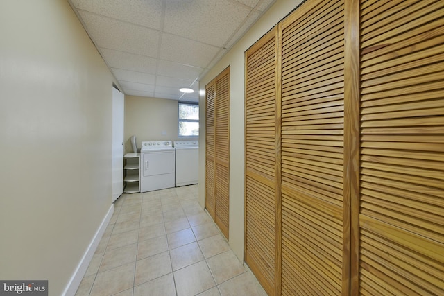 hall with washer and clothes dryer, a drop ceiling, and light tile patterned flooring