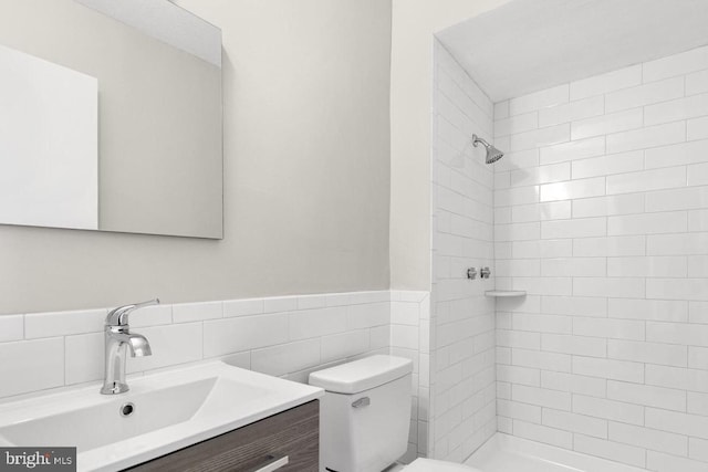 bathroom with tile walls, toilet, tiled shower, and vanity