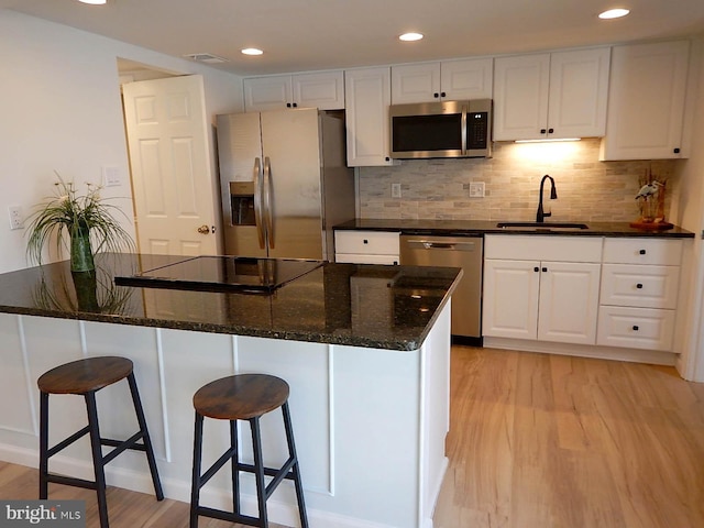 kitchen featuring white cabinetry, sink, dark stone countertops, light hardwood / wood-style floors, and appliances with stainless steel finishes