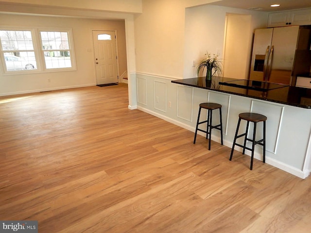 interior space featuring stainless steel fridge, black electric cooktop, light hardwood / wood-style floors, a kitchen bar, and kitchen peninsula