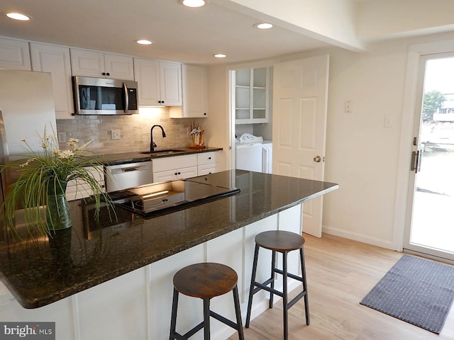 kitchen featuring a kitchen bar, stainless steel appliances, sink, separate washer and dryer, and white cabinetry