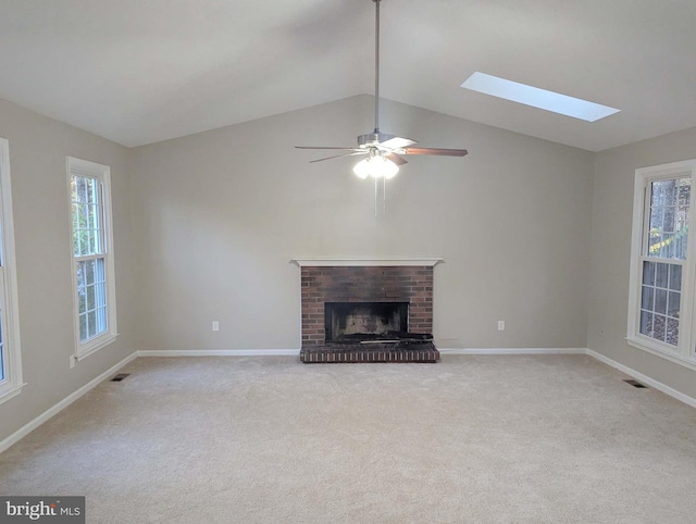 unfurnished living room with ceiling fan, light carpet, lofted ceiling with skylight, and a brick fireplace