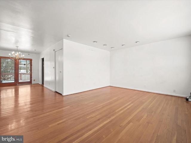 empty room with wood-type flooring and an inviting chandelier