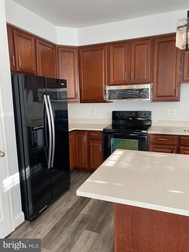 kitchen featuring light stone countertops, black appliances, range hood, and wood-type flooring