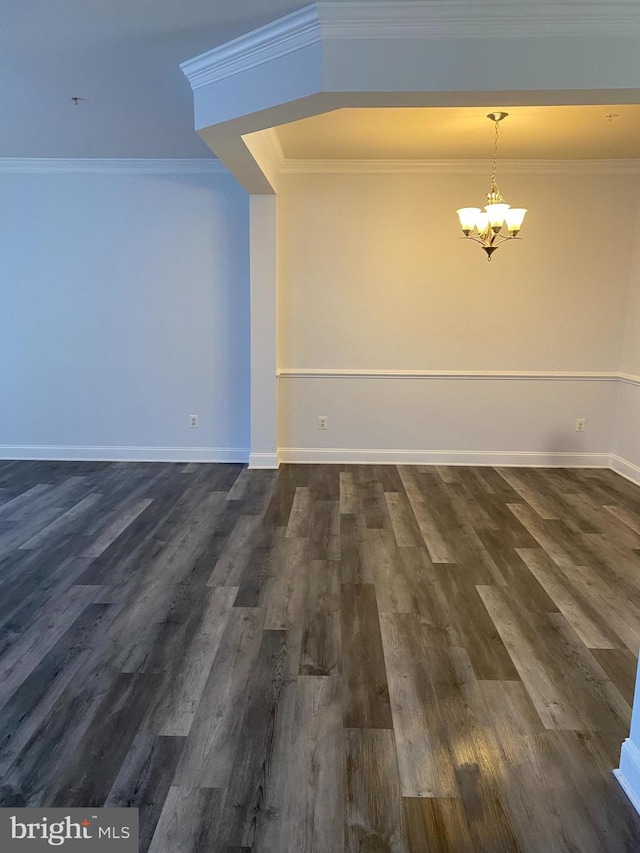 spare room featuring ornamental molding, dark wood-type flooring, and an inviting chandelier