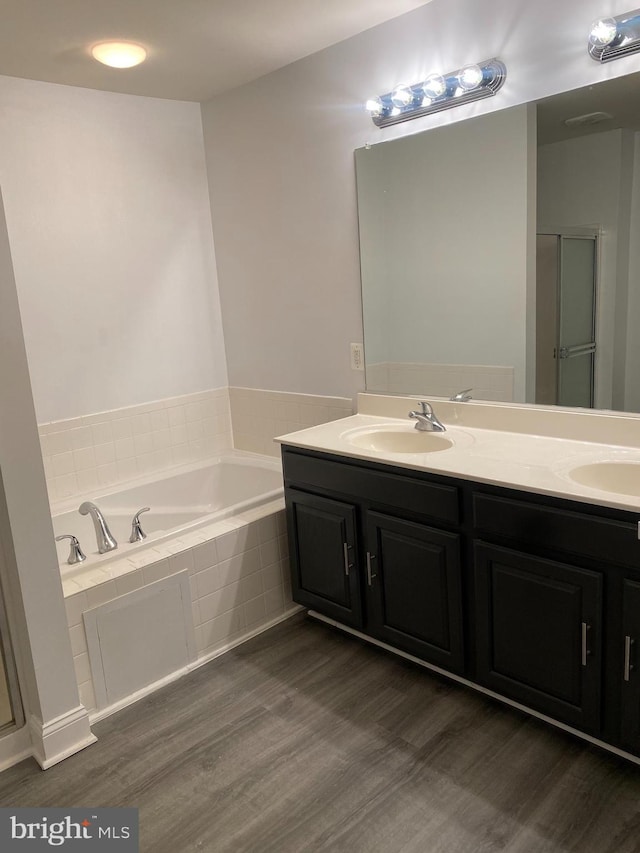 bathroom featuring hardwood / wood-style floors, vanity, and tiled tub