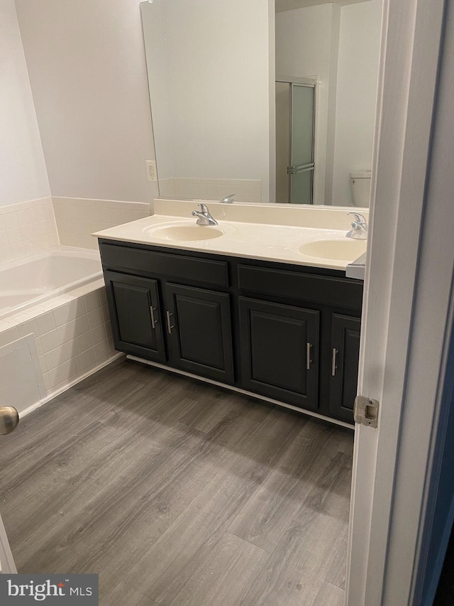 bathroom featuring wood-type flooring, vanity, toilet, and tiled tub