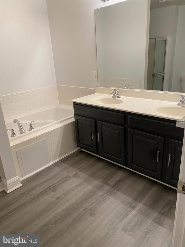 bathroom with hardwood / wood-style floors, vanity, and tiled tub