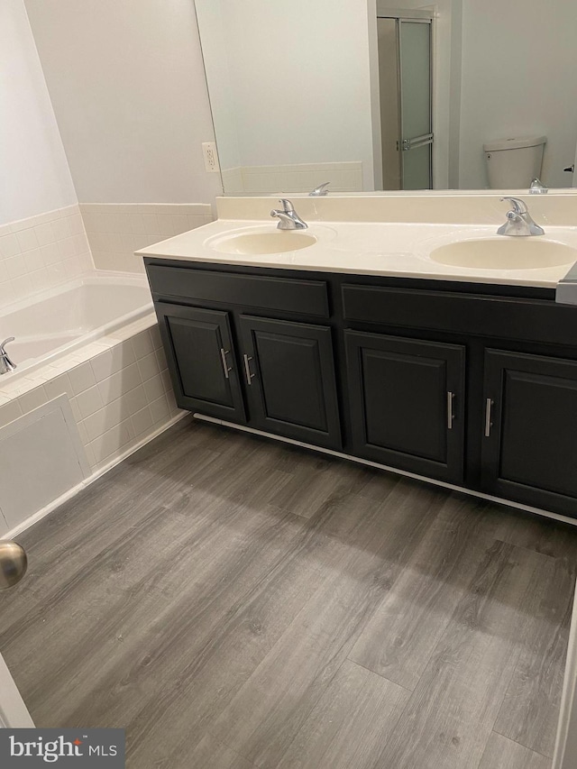 bathroom with tiled bath, hardwood / wood-style floors, vanity, and toilet