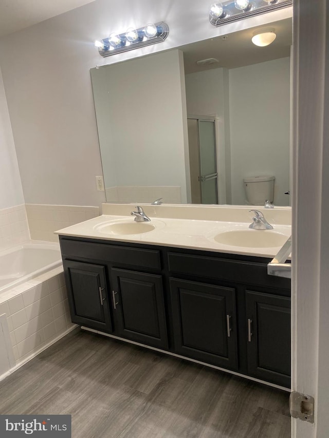 bathroom featuring vanity, toilet, wood-type flooring, and tiled tub