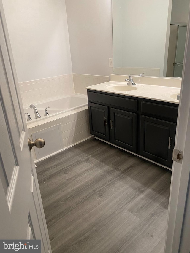 bathroom with vanity, a relaxing tiled tub, and wood-type flooring