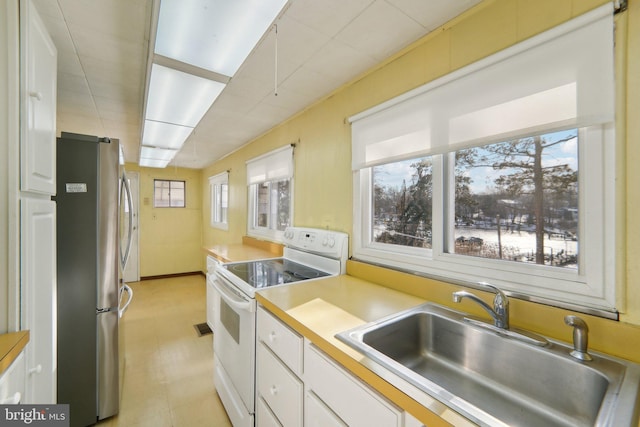 kitchen with white cabinetry, sink, stainless steel refrigerator, and white range with electric cooktop