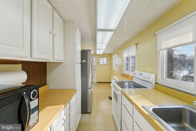 kitchen with stainless steel fridge, sink, white electric range oven, and white cabinets