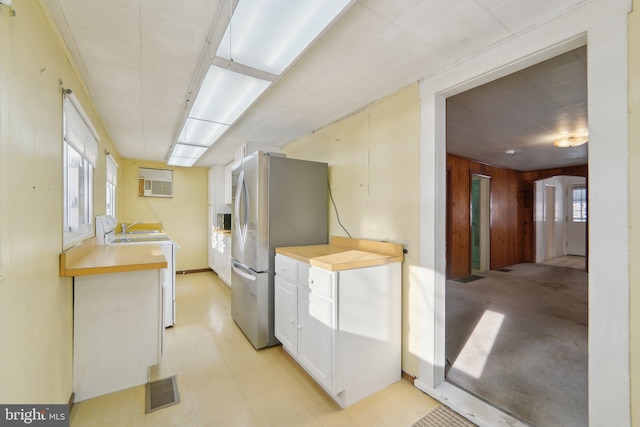 kitchen with white electric stove, white cabinets, stainless steel fridge, and wooden walls