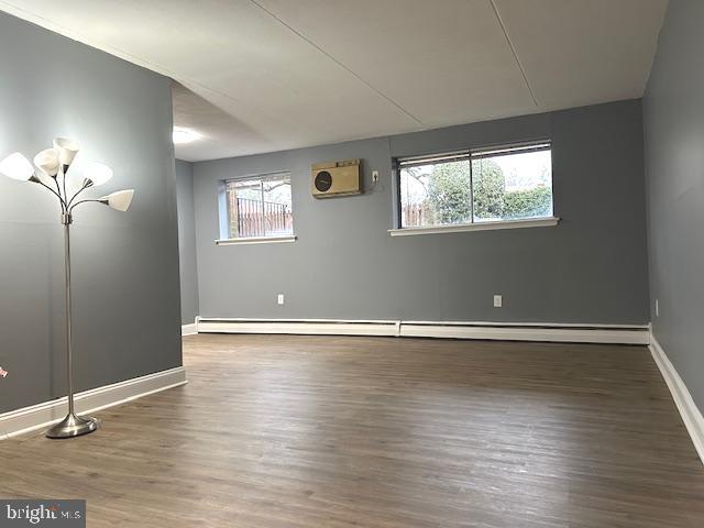 unfurnished room featuring a wall mounted AC, dark hardwood / wood-style flooring, and baseboard heating