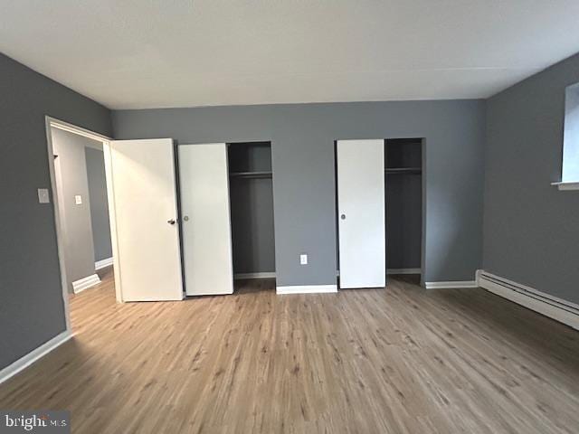 unfurnished bedroom featuring two closets, light hardwood / wood-style flooring, and a baseboard radiator