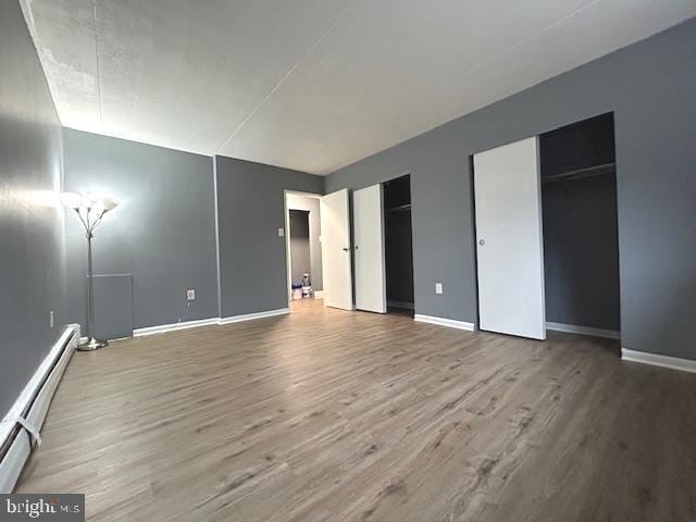 unfurnished bedroom featuring hardwood / wood-style flooring, multiple closets, and a baseboard heating unit