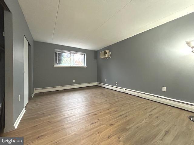 spare room with baseboard heating, a wall mounted AC, and wood-type flooring