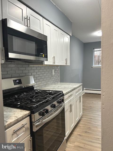 kitchen with light stone countertops, baseboard heating, light hardwood / wood-style flooring, white cabinets, and appliances with stainless steel finishes